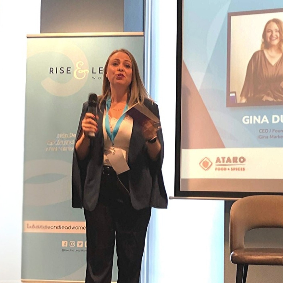 Gina Dunn, brand strategist and founder, speaking on stage at a Rise and Lead Women event, holding a microphone