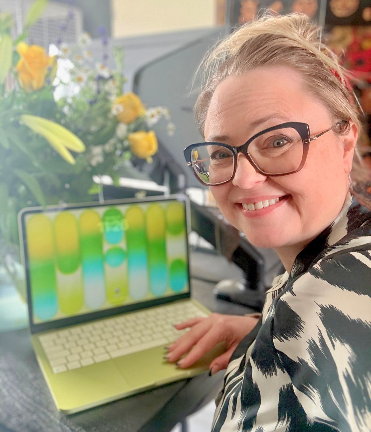 Gina Dunn, brand strategist and founder of OG Solutions in Almere, smiling at her desk with a green laptop and yellow